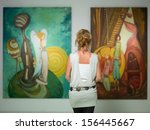 rear view of younga caucasian woman stading in an art gallery in front of two large colorful paintings
