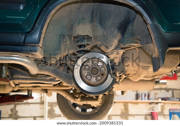 Rear wheel hub of a car\
lifted on a lift. In the garage, a man changes parts on a vehicle.\
Small business concept, car repair and maintenance service. UHD\
4K.