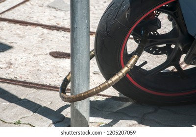 Rear Wheel Of Powerful Motorcycle Locked With Chain Bike Lock To Road Sign Pole Closeup In Sunny Day