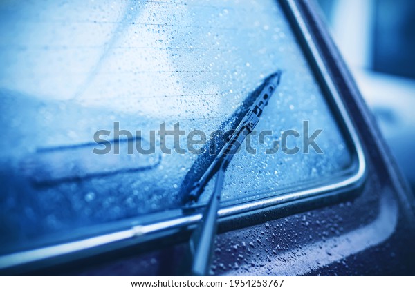The rear window of the car and the black\
windshield wiper are covered with drops of heavy rain in cloudy\
dark weather. Bad weather.