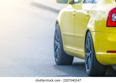 Rear Of A Yellow Modern Sports Car In Selective Focus At Sunset While Driving On The Road. Taken In Backlit And Sun Glare.