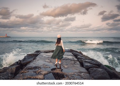 Rear of young asian woman standing and posing on jetty rocks and wave hitting on Jumunjin beach at Gangneung, South Korea