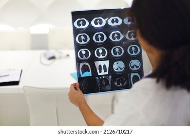 Rearview Of Ethnic Female Doctor Analyzing X-ray Or MRI Scan While Working In Hospital, Selective Focus. Physician Looking At CT Screening, Using Diagnostic Tool For Detecting Lung Diseases