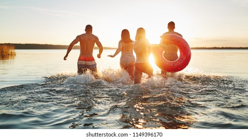 Rearview of a group of diverse young friends in swimsuits splashing water while running into a lake together on a late summer afternoon - Powered by Shutterstock