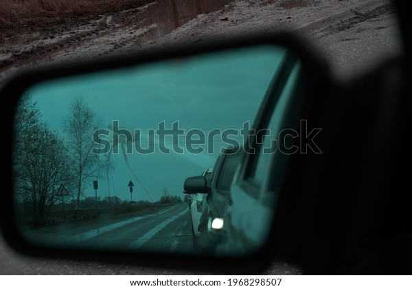A rear-view mirror with an anti-reflective\
coating. Cars stand in a row, queue. In the background you can see\
a tripod unidentified robot that shines the headlight to the side.\
Rainy, foggy weather.