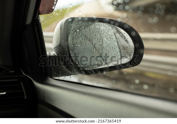 Rear-view mirror in car. Car window in\
rain. Transport details. Raindrops on rearview\
mirror.