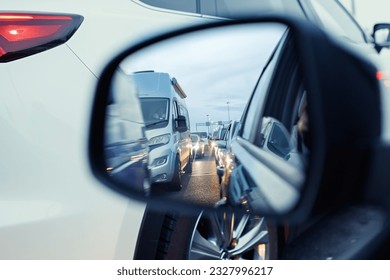 in the rearview mirror in the evening, cars with headlights are queuing in a traffic jam