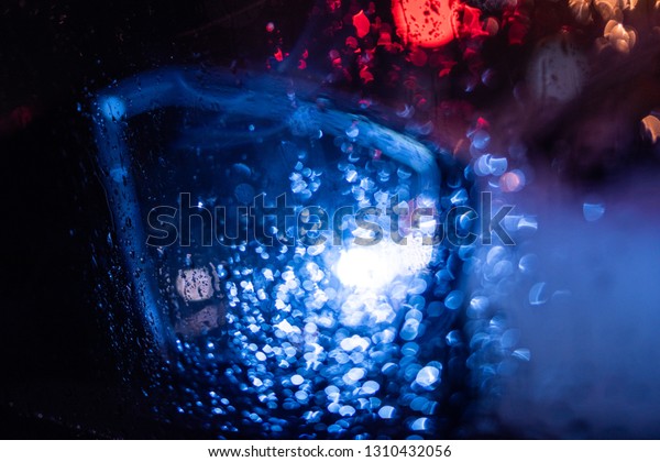 Rear-view\
mirror point of view pov personal perspective on modern new\
electric luxury car driving in the city with defocused bokeh lights\
on a stormy rainy night - blue color\
cast