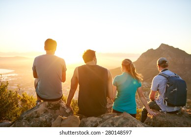 Rearview Of A Row Of Friends Sitting On A Nature Trail Watching The Sunrise Together