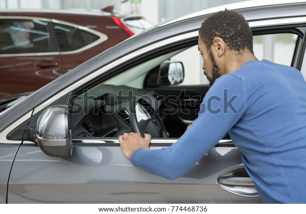 Rearview shot of an African man examining a new car\
at the dealership looking inside the automobile copyspace interior\
modern auto automotive vehicle transport driving comfort luxury\
consumerism sale