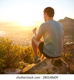 Rearview Shot Of A Young Guy On A Nature Trail Pausing To Eat A Protein Bar While Watching The Sunrise