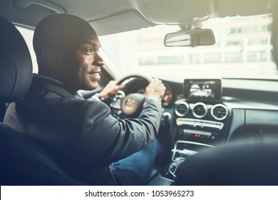 Rearview Of A Smiling African Businessman Driving His Car During His Morning Commute To Work Through The City