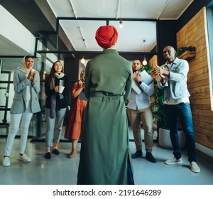 Rearview Of A Successful Businesswoman Receiving An Applause From Her Colleagues In A Modern Office. Muslim Businesswoman Giving A Speech During A Staff Meeting In A Multicultural Workplace.