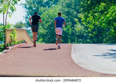 Rearview Of Two Male Friends Running Outdoors In A Park