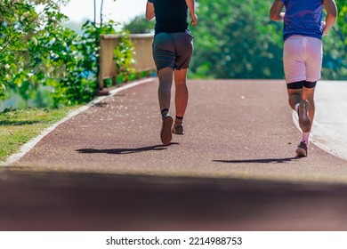 Rearview Of Two Male Friends Running Outdoors In A Park