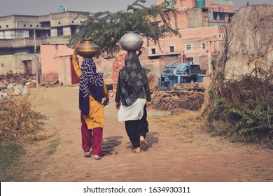 Rearview Of Two Women Carrying Water Pots On Their Head In Village Area