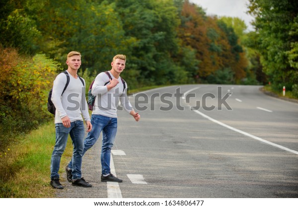 Reason people pick up hitchhikers. Missed their bus.\
Need help. Cheap transport. Transport problem. Travel and transport\
concept. Twins men at edge of road nature background. Try to stop\
some car.