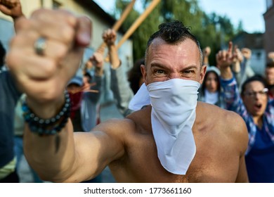 Rebellious Man With Face Mask Protesting With Crowd Of People On City Streets And Looking At The Camera. 