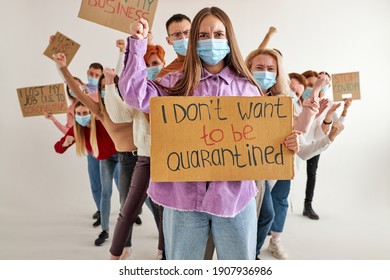 Rebellious Woman Standing With Cardboard Asking Not To Be Quarantined, Tired Of Sitting At Home. Many People Stand Behind Her Back Looking At Camera, Wearing Medical Masks. Isolated