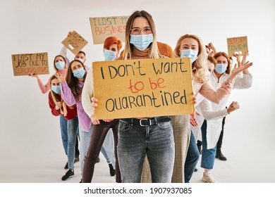 Rebellious Woman Standing With Cardboard Asking Not To Be Quarantined, Tired Of Sitting At Home. Many People Stand Behind Her Back Looking At Camera, Wearing Medical Masks. Isolated