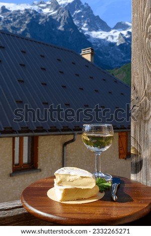 Reblochon French cheese made in Haute-Savoie, white Roussette de Savoie or Vin de Savoie wine with view on old alripne village and Hautes Alpes mountains snow tops in summer.