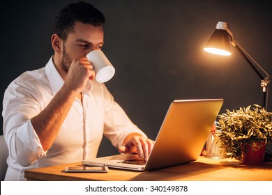 Rebooting his energy to work more. Confident young man drinking coffee while sitting at his working place at night time - Powered by Shutterstock