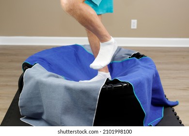 Rebounder or mini trampoline, small round and black being jogged on by an adult white male. Lower legs of an adult white male exercising on a round black rebounder or mini trampoline with two towels.