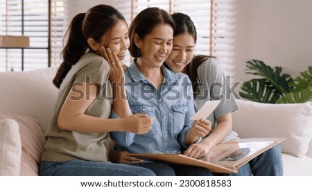 Recall the past life memories Happy time Mother's day grown up kid child joy fun look at old retro photo album with mature mum. Asia adult people middle age mom smile enjoy relax sitting at home sofa.