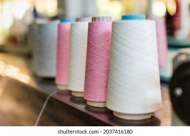 Receding Line Of Alternating Reels Of Pink And White Cashmere Yarn In A Knitwear Factory With Selective Focus To A Pink Spool