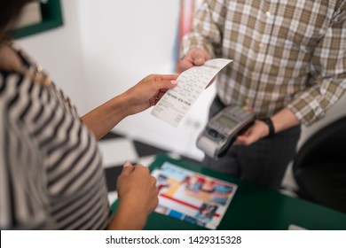 The receipt in hands. Close-up photo of seller handing the receipt to the customer during purchasing process.