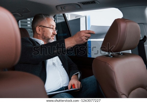 Receiving the contract.\
Paperwork on the back seat of the car. Senior businessman with\
documents.