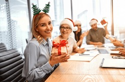 Receiving Gifts At Work Is A Pleasure. Adult Beautiful Happy Smiling Woman With Ears With A Christmas Tree Holding A Christmas Present And Laughing Looking At The Camera.