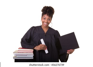 Recent College Graduate In A Cap And Gown Next To A Stack Of Books Isolated On White