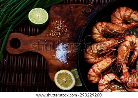 Recent large king prawns cooked in a pan, lay next to lemon and lime, rosemary and chives, Best fried shrimp appetizer to the cold beer