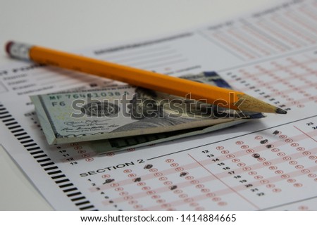 Recent scandals of bribery of college officials to admit wealthy students has plagued many college admissions offices. Image of a pencil lying on a SAT exam answer sheet and one hundred dollar bill.