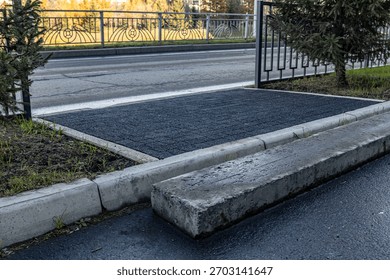 Recently asphalted small asphalt patch between concrete barriers. Newly laid sidewalk, pavement. Urban street curb, metal decorative fence along quiet road with a park. Street, city life, and infrastr