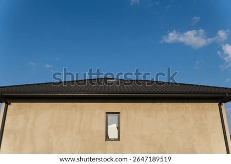 A recently built home features a smooth plaster exterior and a dark tiled roof under a brilliant blue sky in the late afternoon.