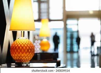 Reception Area In Luxury Hotel Close Up On Lamp With People Traveling In And Out The Front Entrance