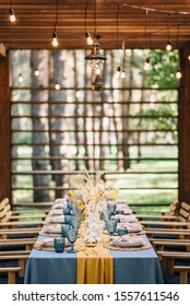 Reception Table Decorated By Flowers, Wheat, Lemons With Hanging Edison Bulb Garland. Wedding. Decor. Yellow And Blue Tablecloth