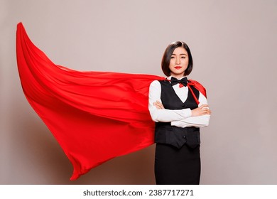 Receptionist with arms crossed wearing red superman cloak, representing power and confidence portrait. Attractive asian waitress dressed in restaurant uniform and fluttering superhero cape - Powered by Shutterstock