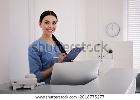 Receptionist with clipboard at countertop in hospital