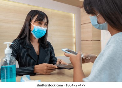 Receptionist And Guest Wearing Face Mask At Front Desk While Having Conversation In Office Or Hospital . Covid 19 And Coronavirus Infection Protection And Protective Policy Concept .