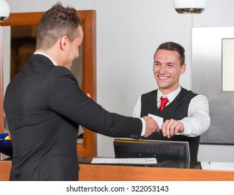 receptionist at hotel reception handing key card to guest or client