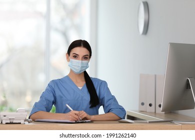 Receptionist With Protective Mask Working At Countertop In Hospital