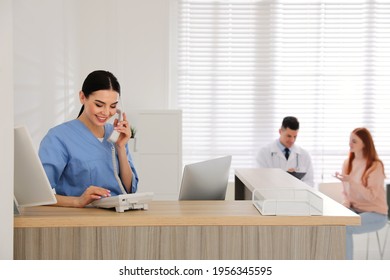 Receptionist talking on phone while doctor working with patient in hospital - Powered by Shutterstock