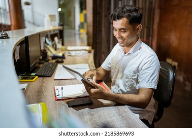 Receptionist Using Digital Tablet While Sitting At Hotel Reception Desk