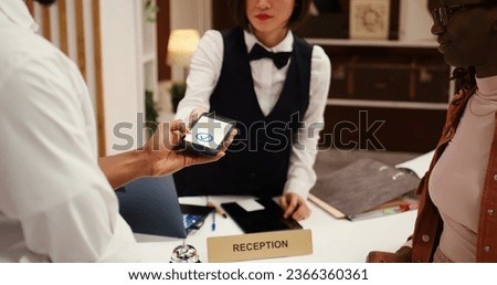 Receptionist using POS payment system to validate card purchase of extra room amenities and hotel services, close up. African american couple using smartphone banking app during booking in process