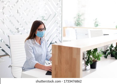 Receptionist Wearing Medical Mask In Office. Protection Employees On Workplace. Young Woman Working At Reception In Hotel. Disease Prevention During Quarantine, Staff Safety.