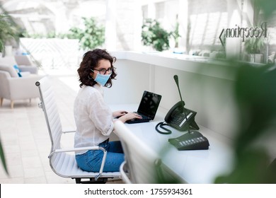 Receptionist Wearing Medical Mask In Office. Protection Employees On Workplace. Woman Working At Reception In Hotel. Social Distancing In Quarantine, Staff Safety. Coronavirus Lockdown Restrictions