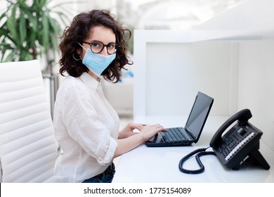 Receptionist Wearing Medical Mask In Office. Protection Employees On Workplace. Young Woman Working At Reception In Hotel. Social Distancing During Coronavirus Quarantine, Staff Safety From Covid 19.